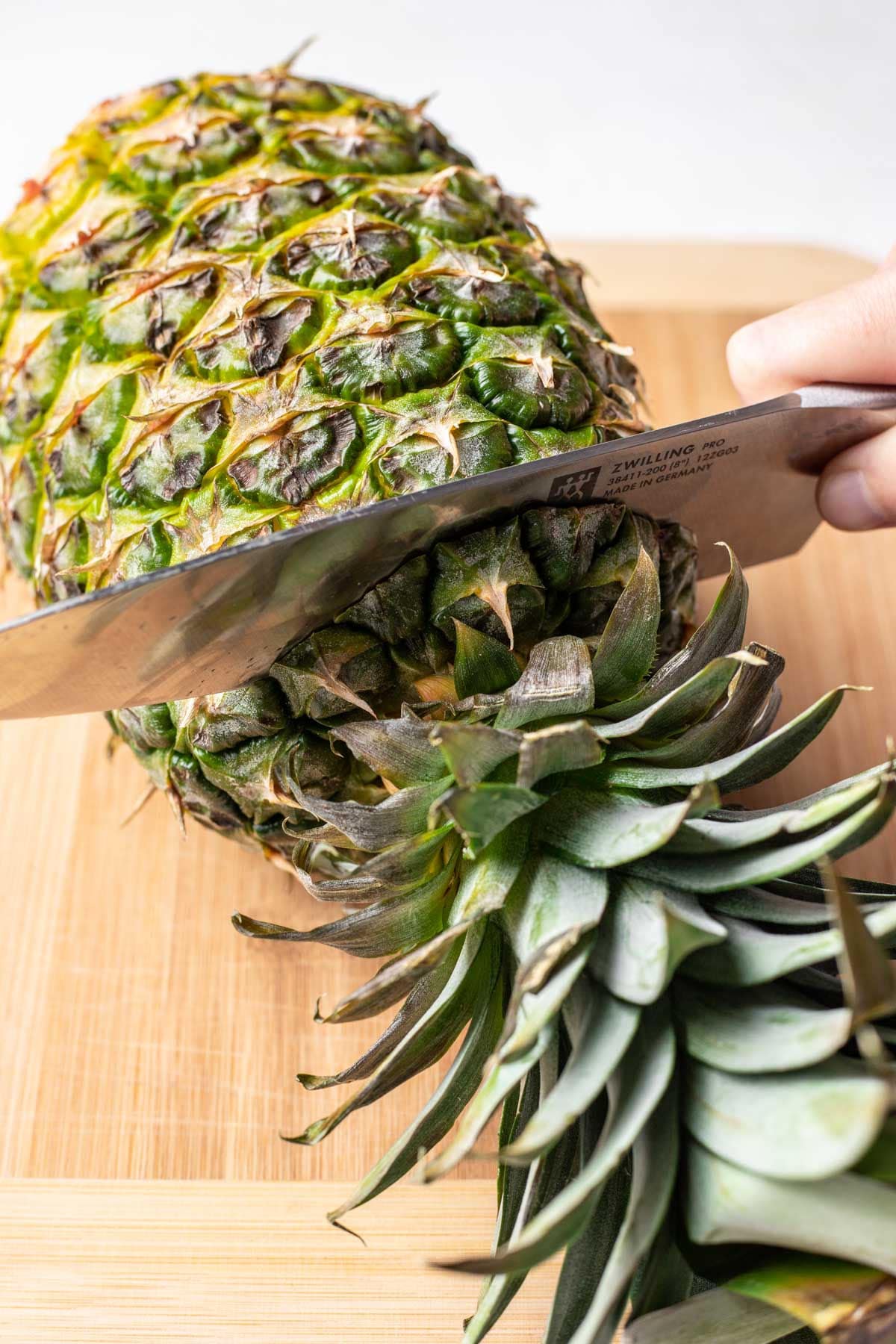 A knife cutting off the top of a pineapple. 