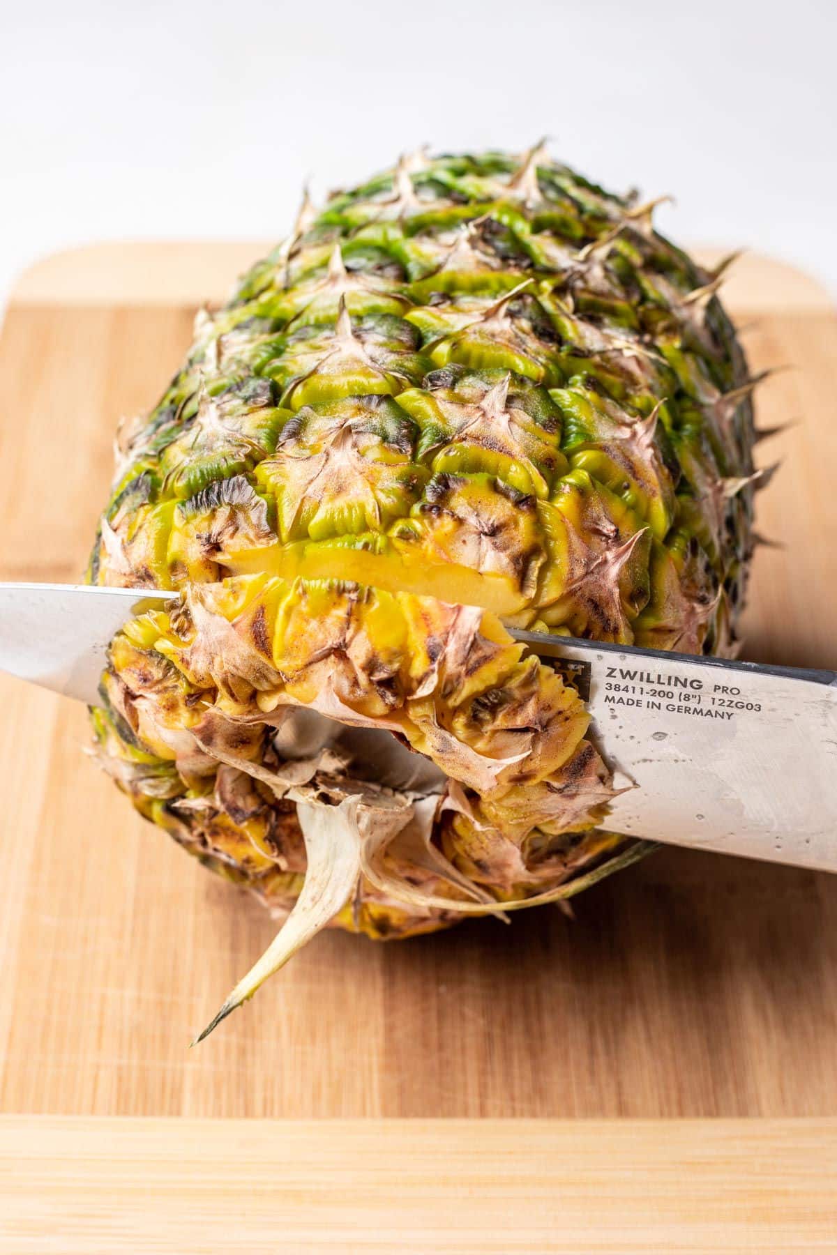 A knife cutting off the bottom of a pineapple. 