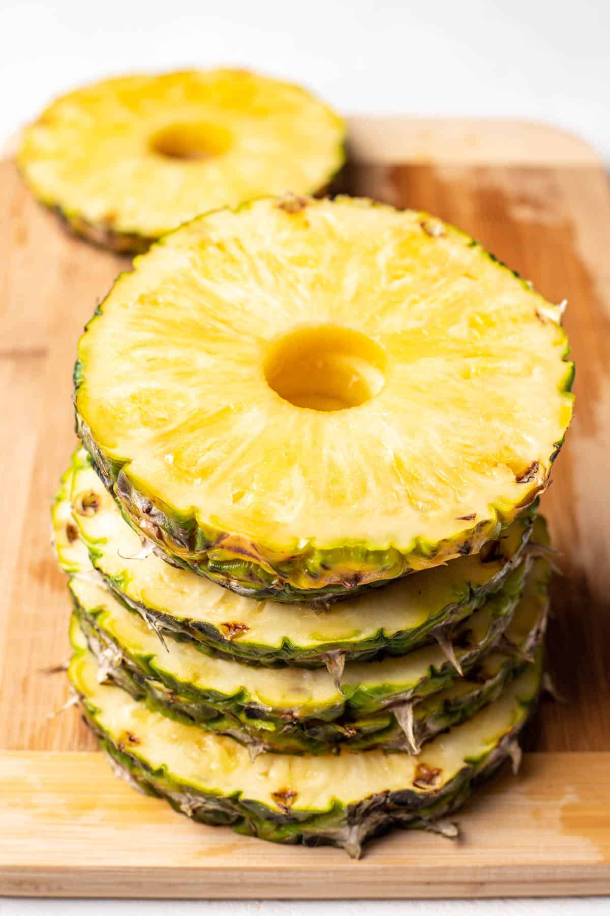 A stack of fresh pineapple rings on a wooden cutting board. 