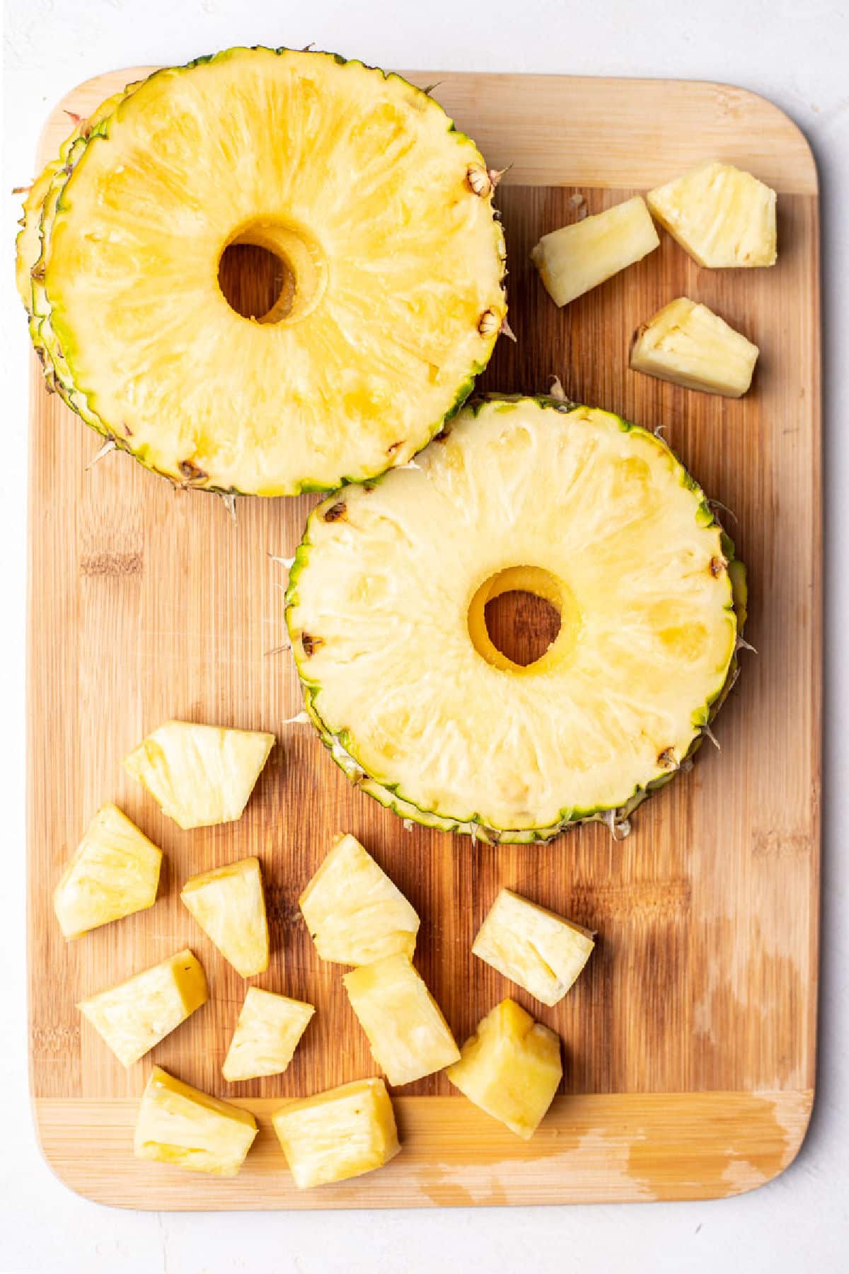 Sliced fresh pineapple rings and pineapple chunks on a wooden cutting board. 