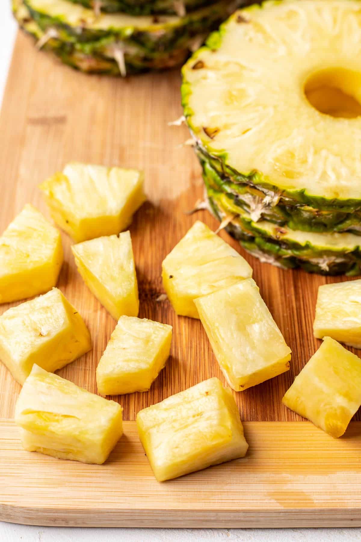 Closer up photo of cut up pineapple chunks on a wooden cutting board. 