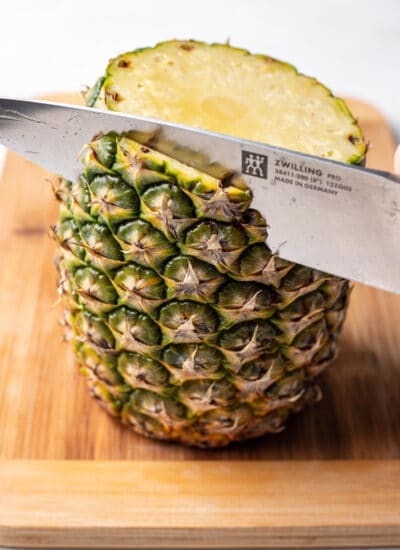 A knife cutting the skin off of a pineapple.
