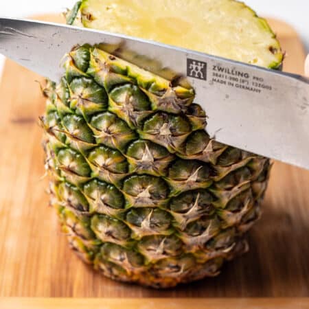 A knife cutting the skin off of a pineapple.