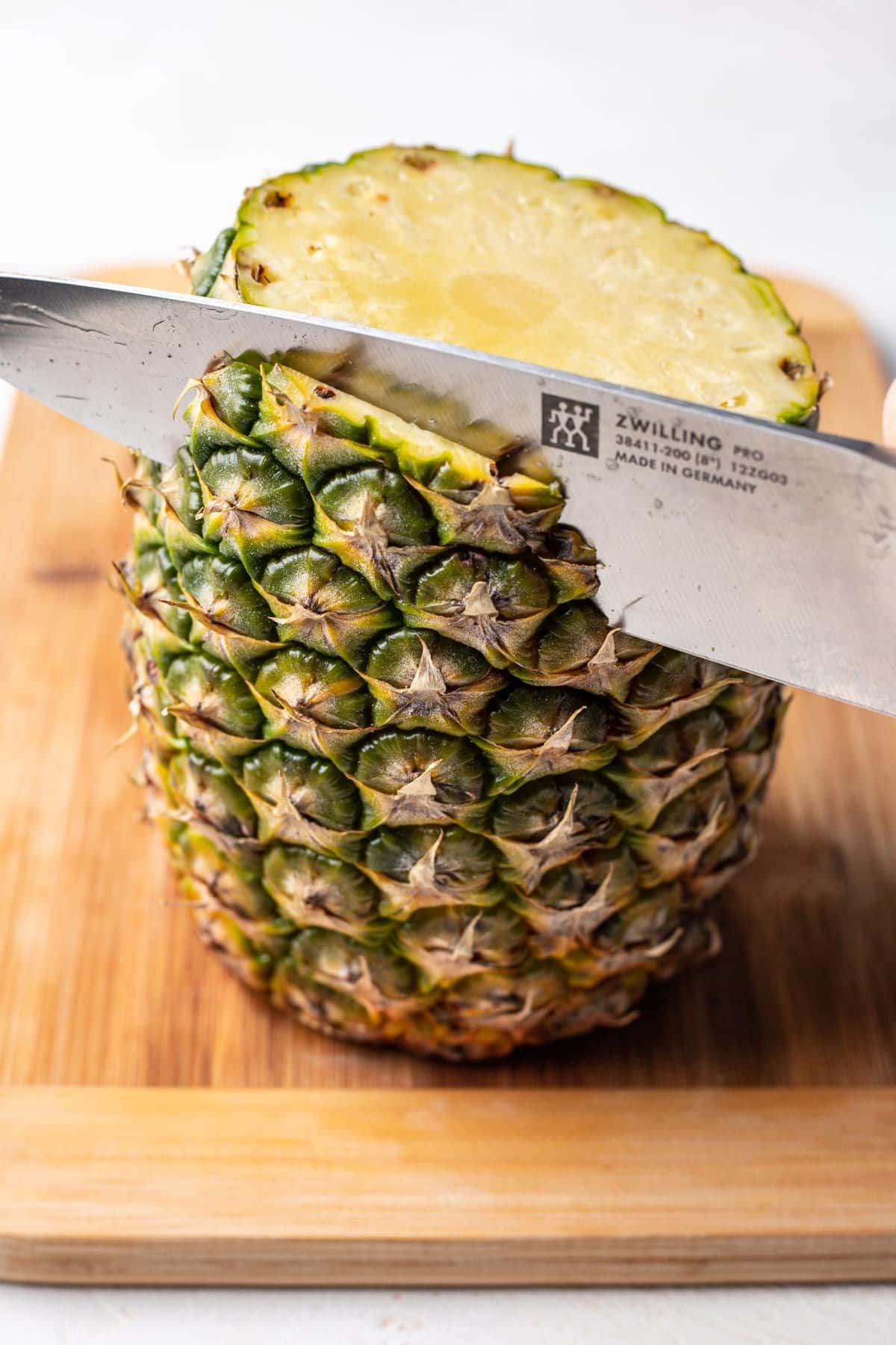 A knife cutting the skin off of a pineapple.