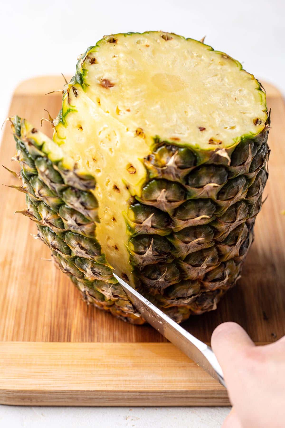 A knife cutting the skin off of a pineapple. 