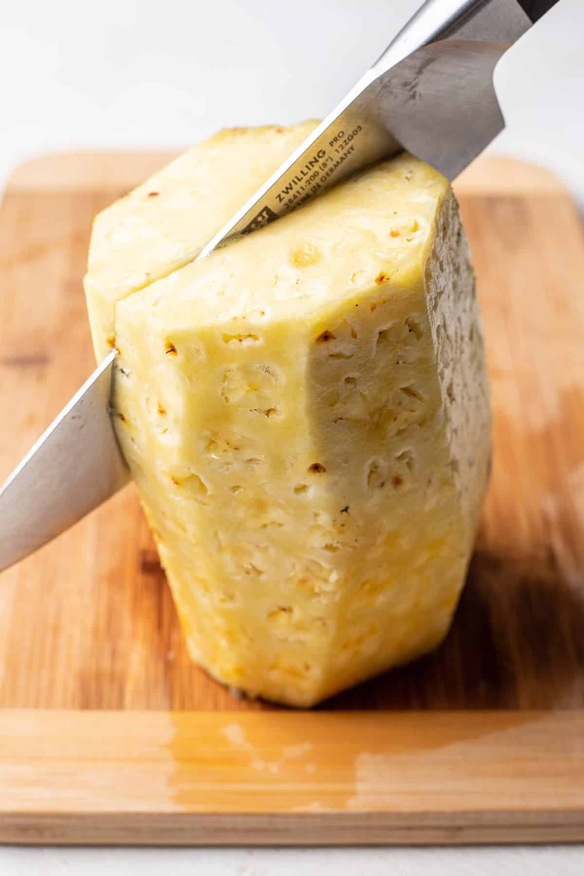 A knife slicing a pineapple in half through the core. 