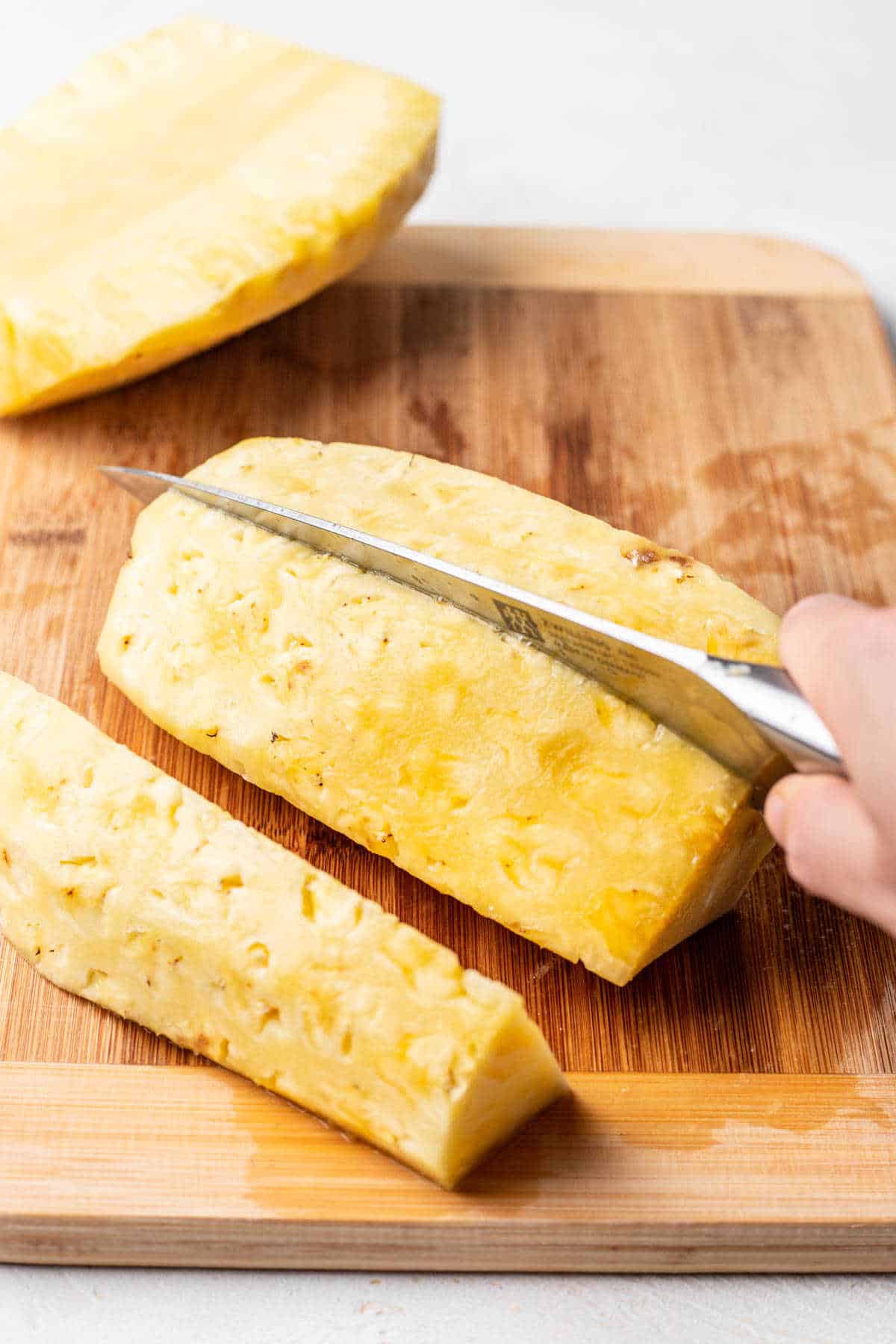 A knife cutting a pineapple half into thirds. 