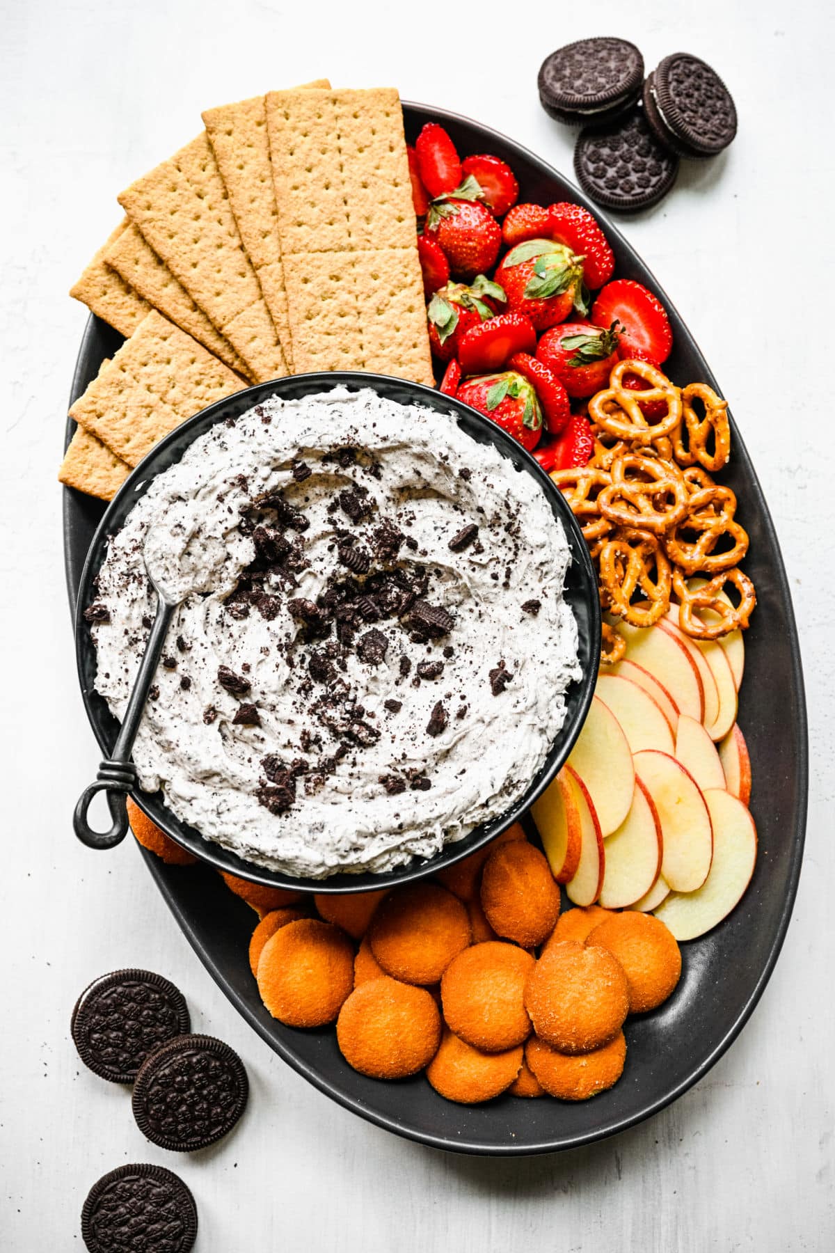 A bowl of Oreo fluff surrounded by graham crackers, fruit, Nilla wafers, and pretzels.