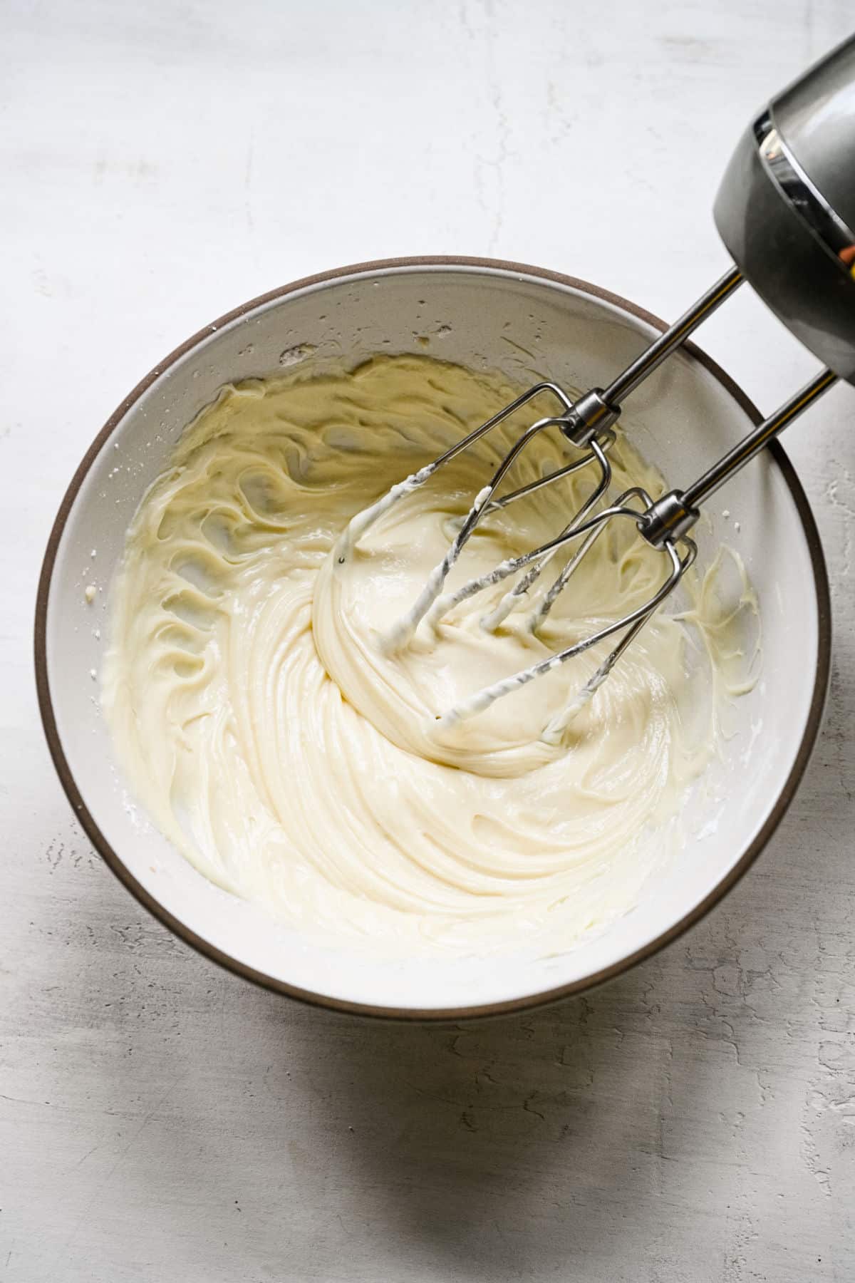 A hand mixer beating cream cheese and powdered sugar together.