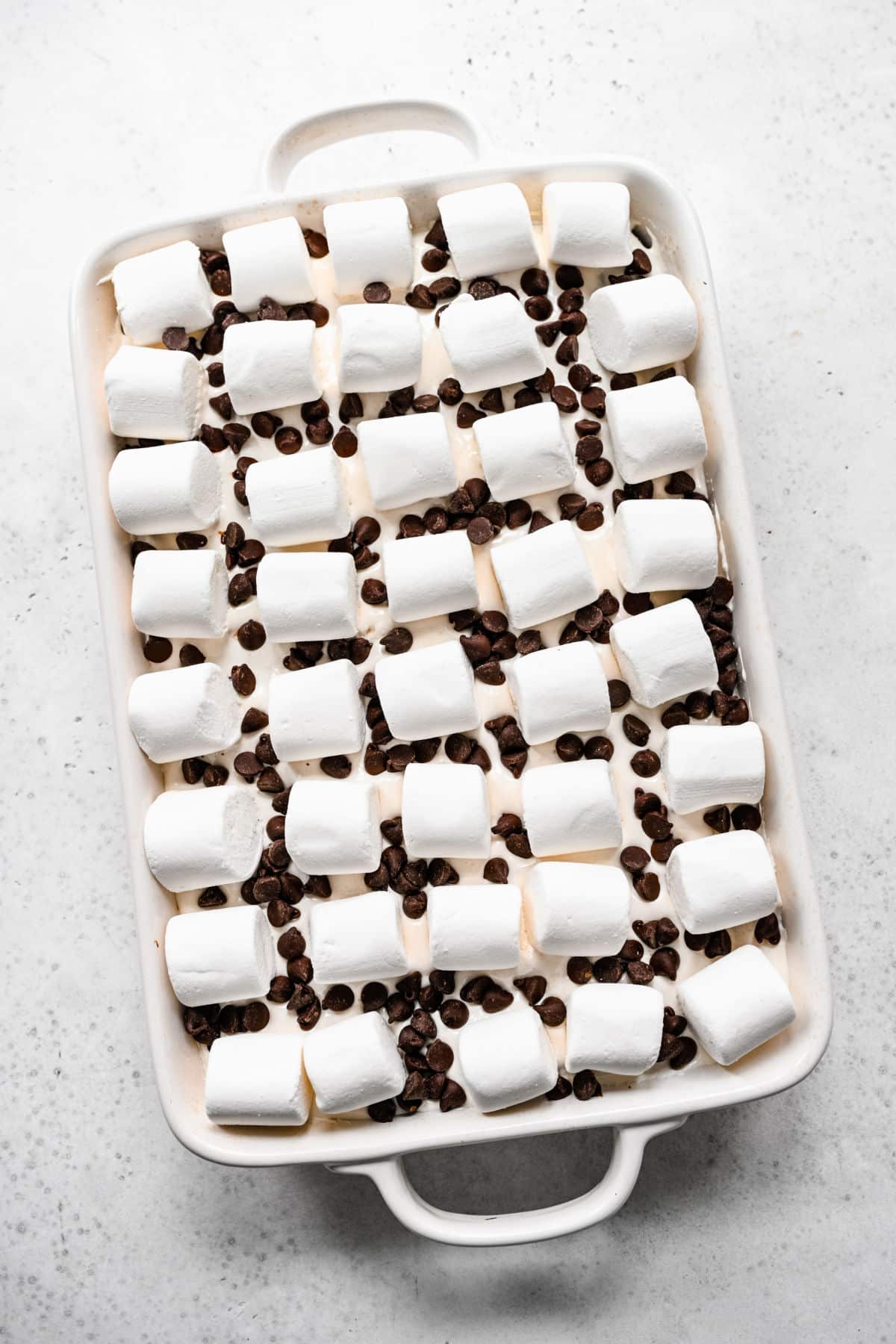 Chocolate chips sprinkled in between large marshmallows on a s'mores cake. 