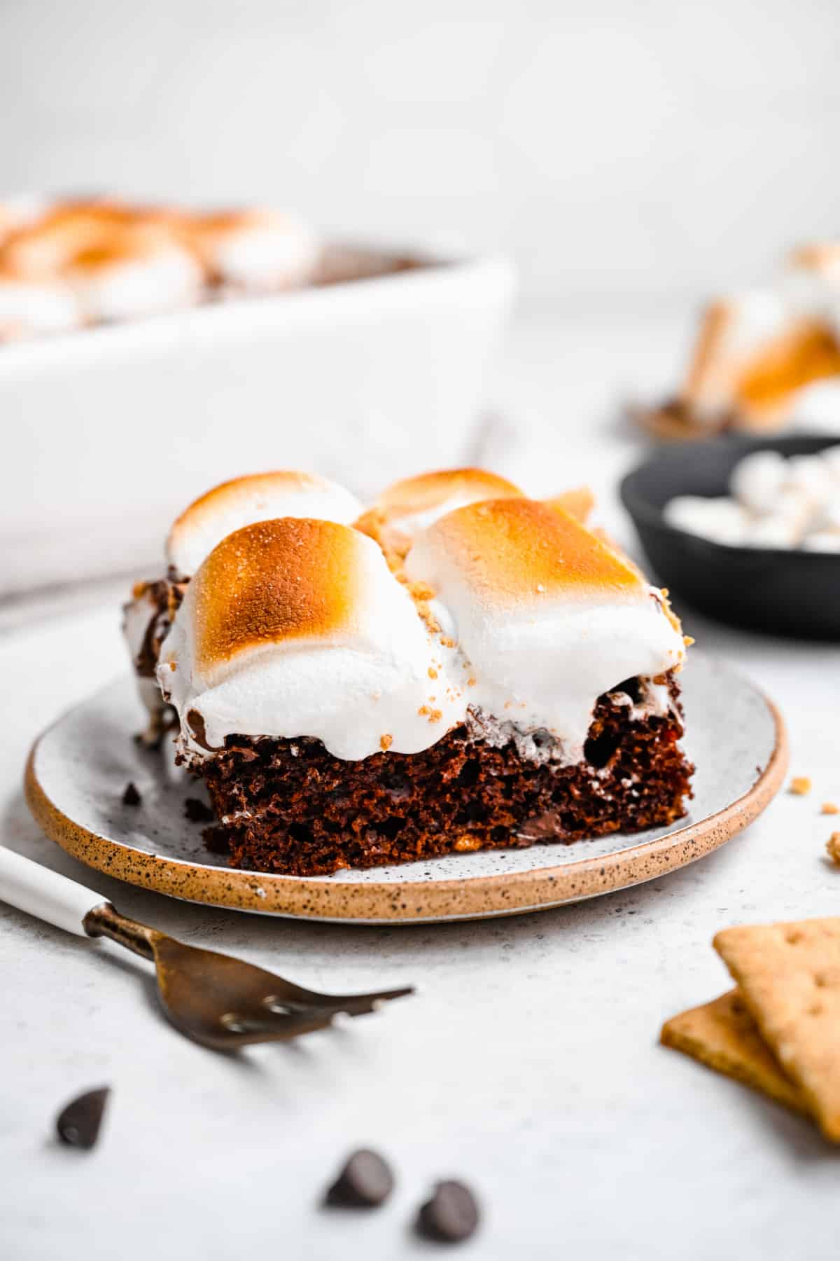 Slices of s'mores cake on plates next to a fork. 