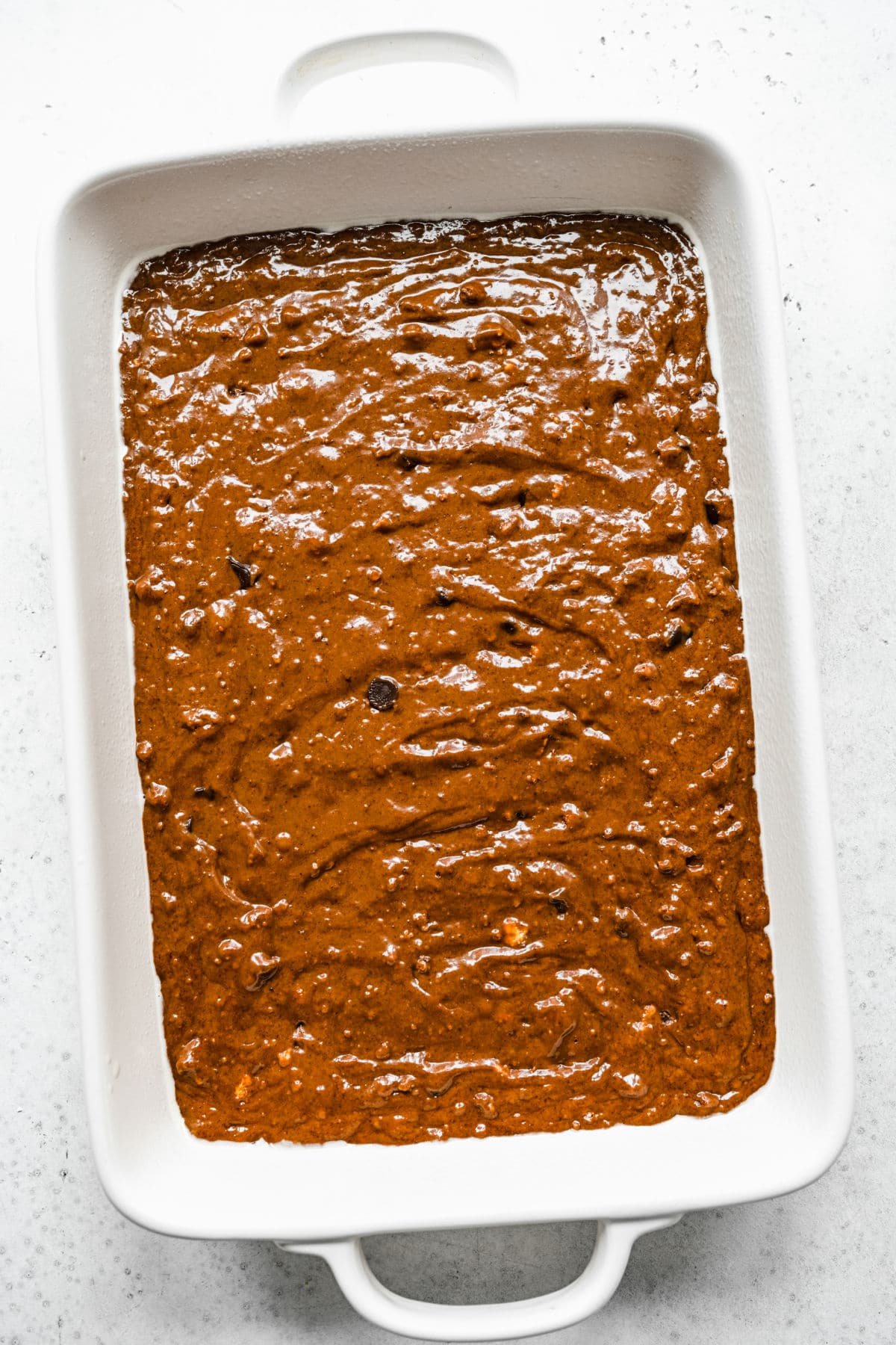 Chocolate cake batter in a white cake pan. 