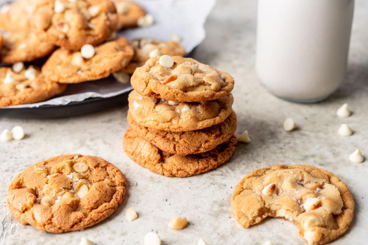 A stack of three white chocolate macadamia cookies next to a plate of cookies.
