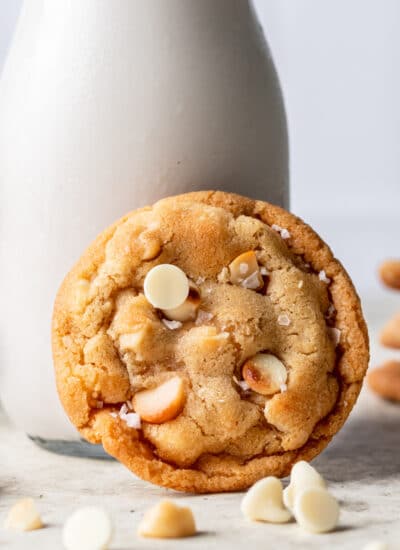 A white chocolate macadamia nut cookie leaning against a bottle of milk.