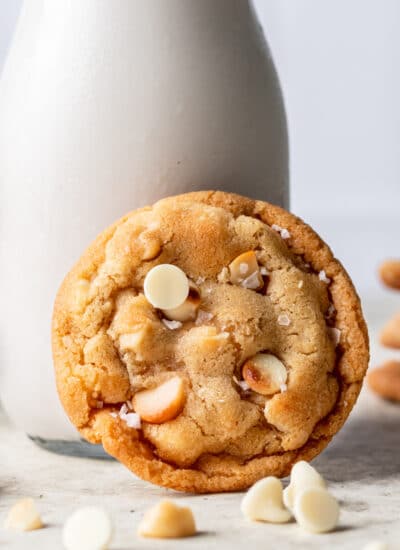 A white chocolate macadamia nut cookie leaning against a bottle of milk.
