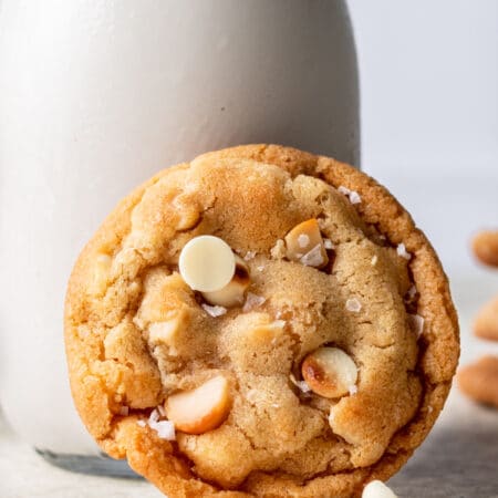 A white chocolate macadamia nut cookie leaning against a bottle of milk.