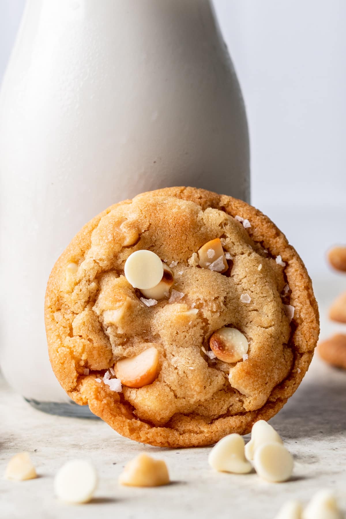 A white chocolate macadamia nut cookie leaning against a bottle of milk.