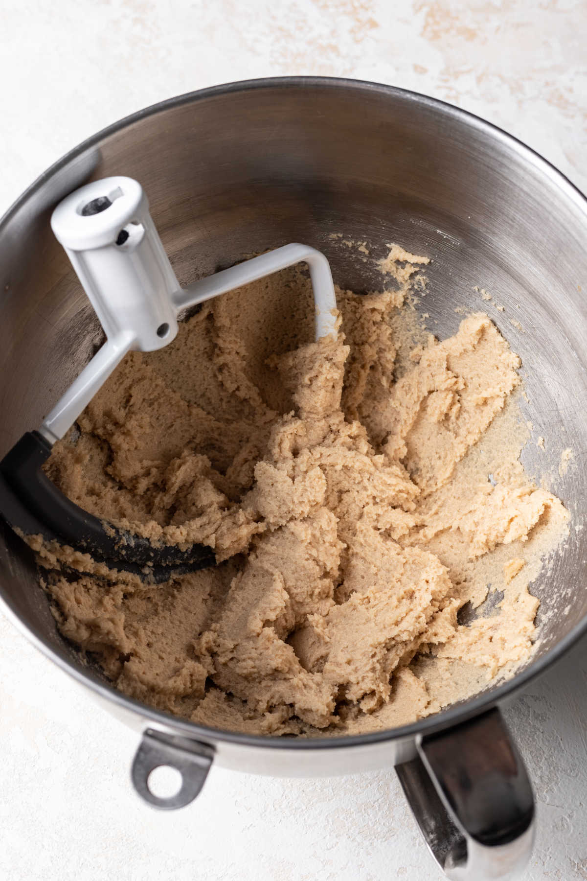 A paddle attachment sitting in creamed butter and sugar mixture. 