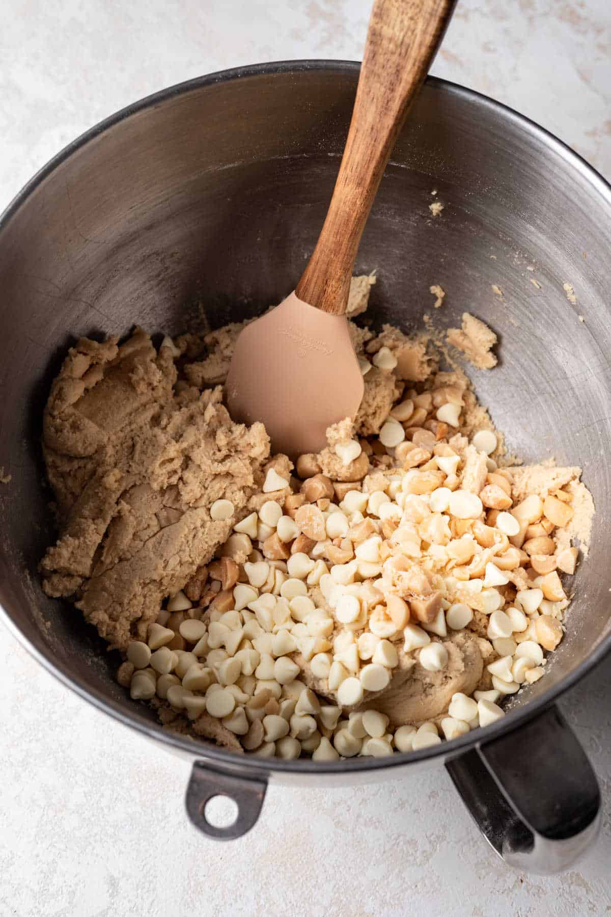 White chocolate chips and macadamia nuts on cookie dough in a mixing bowl. 