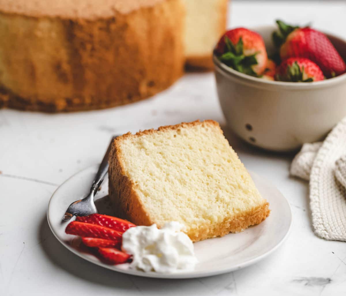 A piece of chiffon cake next to a dish of strawberries. 