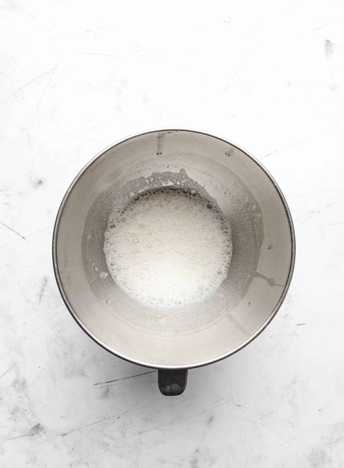 Egg whites and cream of tartar in a silver mixing bowl. 