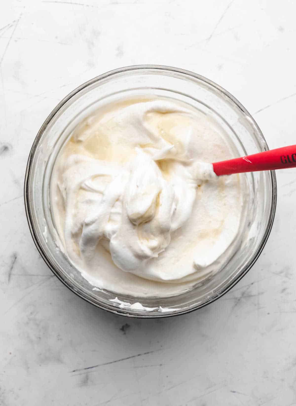 Beaten egg whites folded into egg yolk mixture in a glass mixing bowl. 