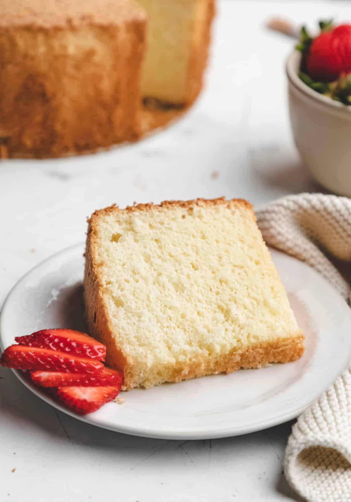 A slice of chiffon cake on a white plate with a sliced strawberry. 
