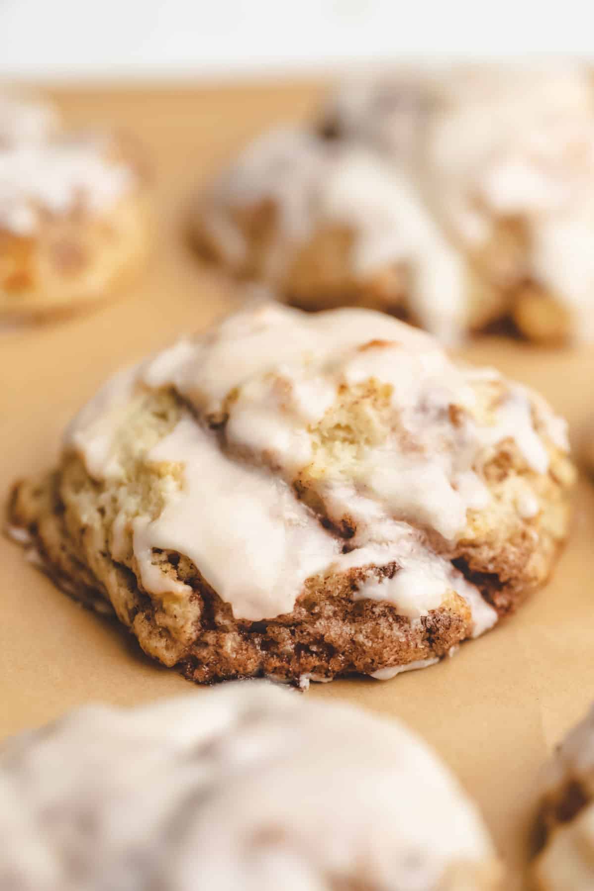 An iced cinnamon swirl biscuit on a piece of brown parchment paper. 