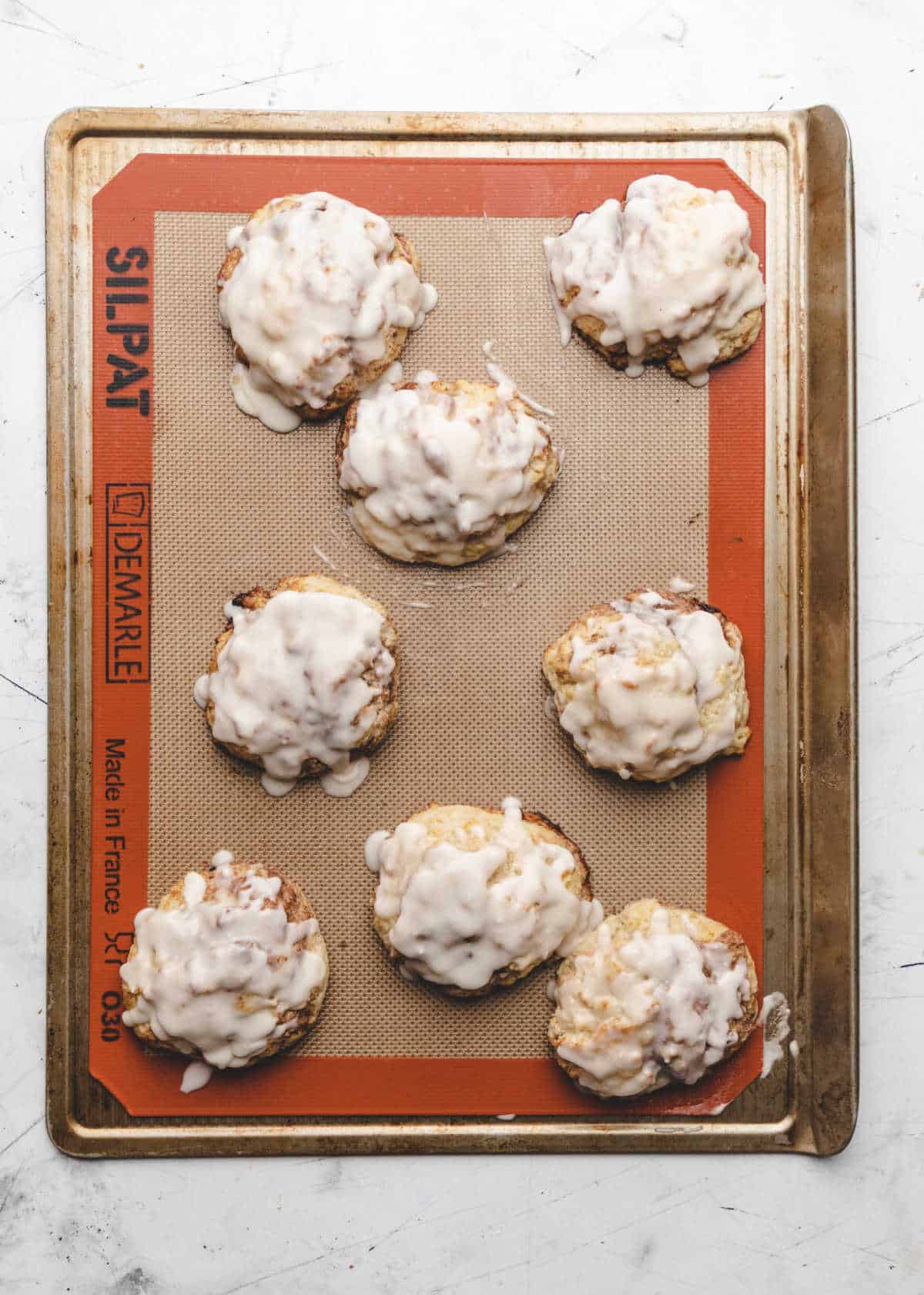 Iced cinnamon swirl biscuits on a baking sheet. 