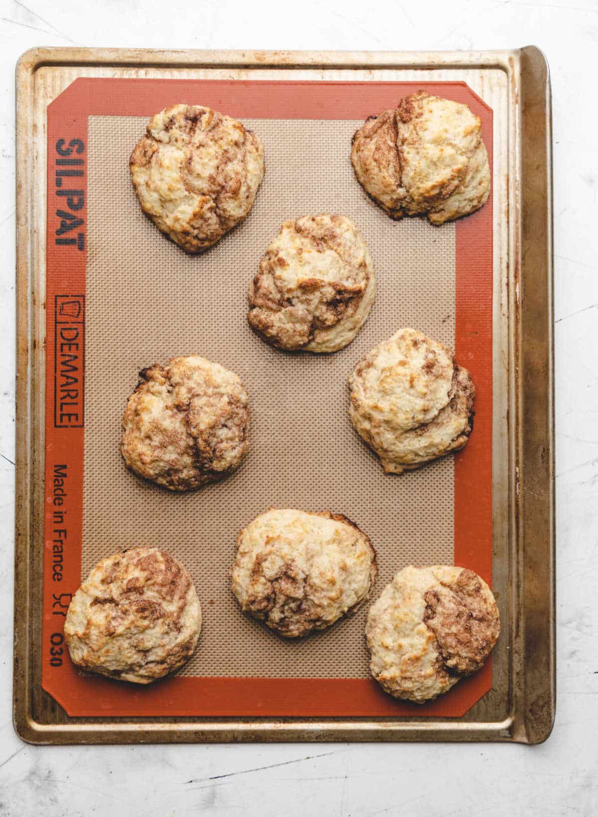 Eight baked cinnamon swirl biscuits on a baking sheet. 