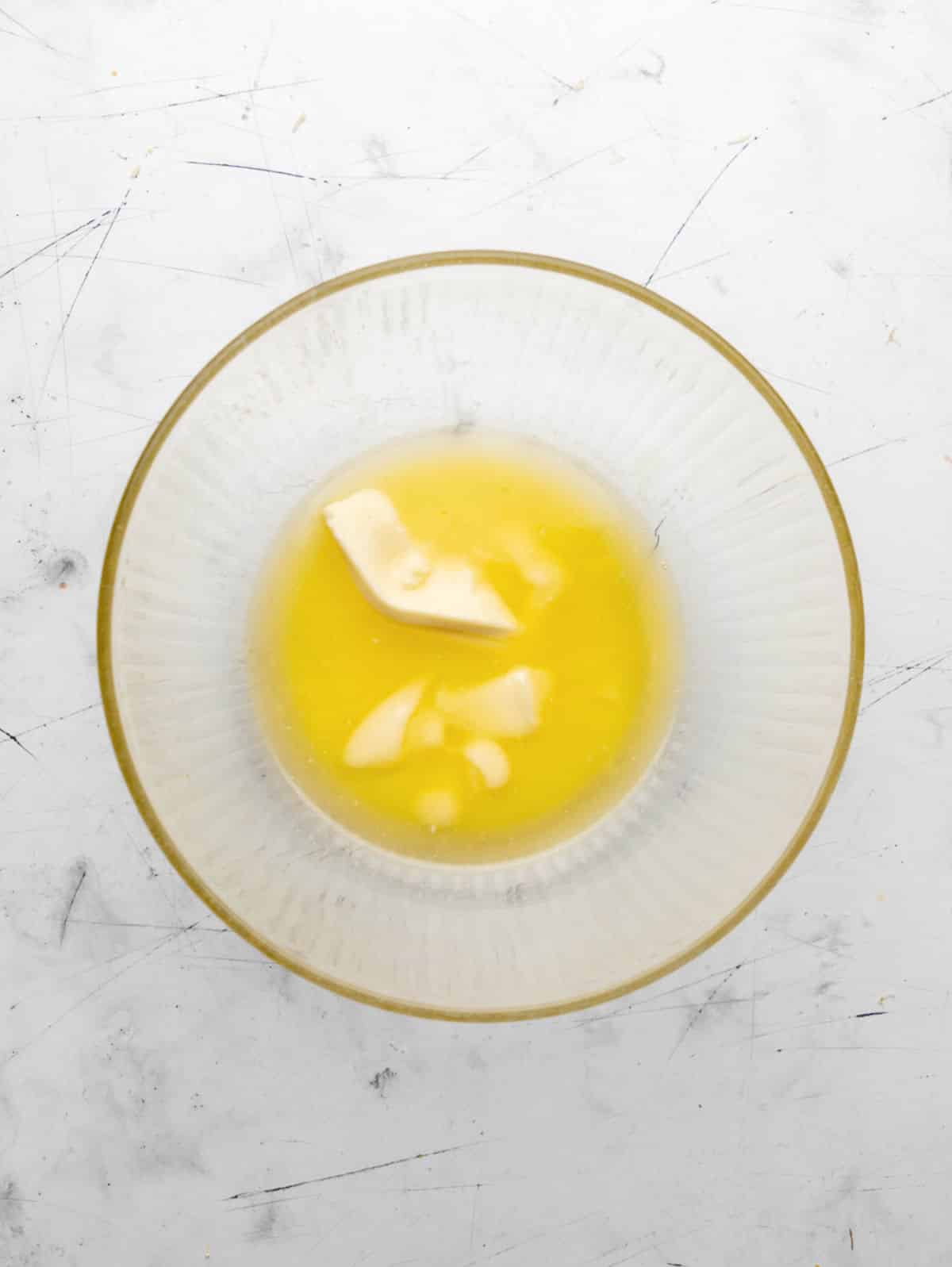 Partially melted butter in a glass mixing bowl.