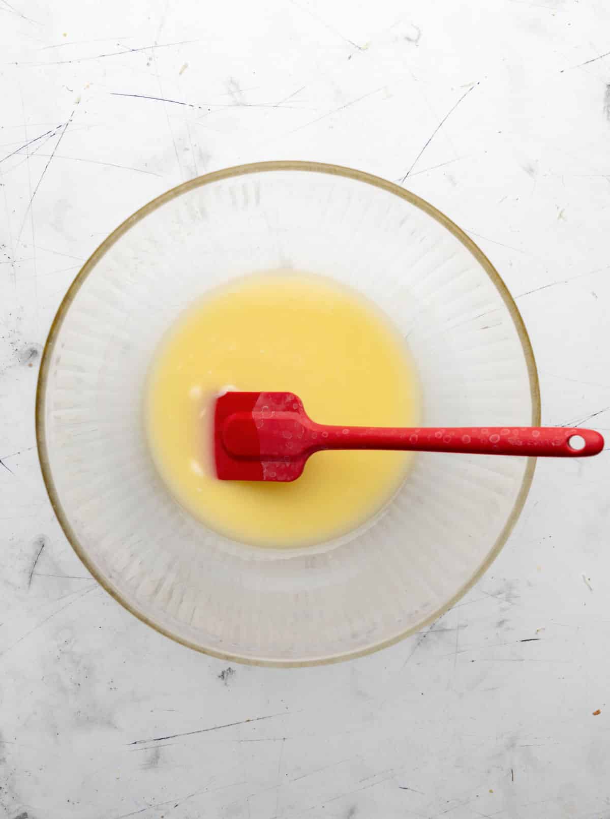 Melted butter in a glass mixing bowl with a red spatula in it. 
