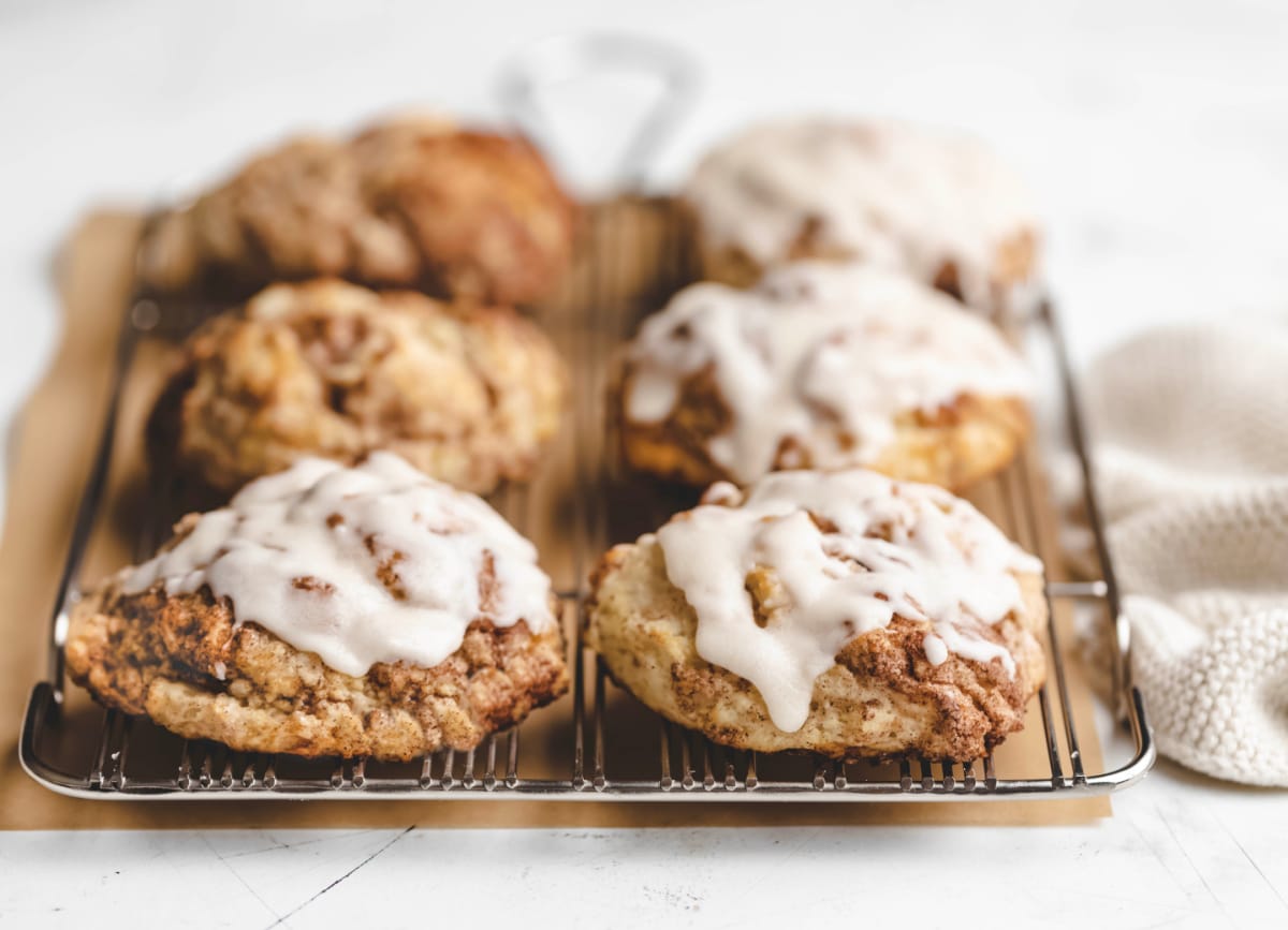 Four iced cinnamon swirl biscuits on a wire cooling rack. 