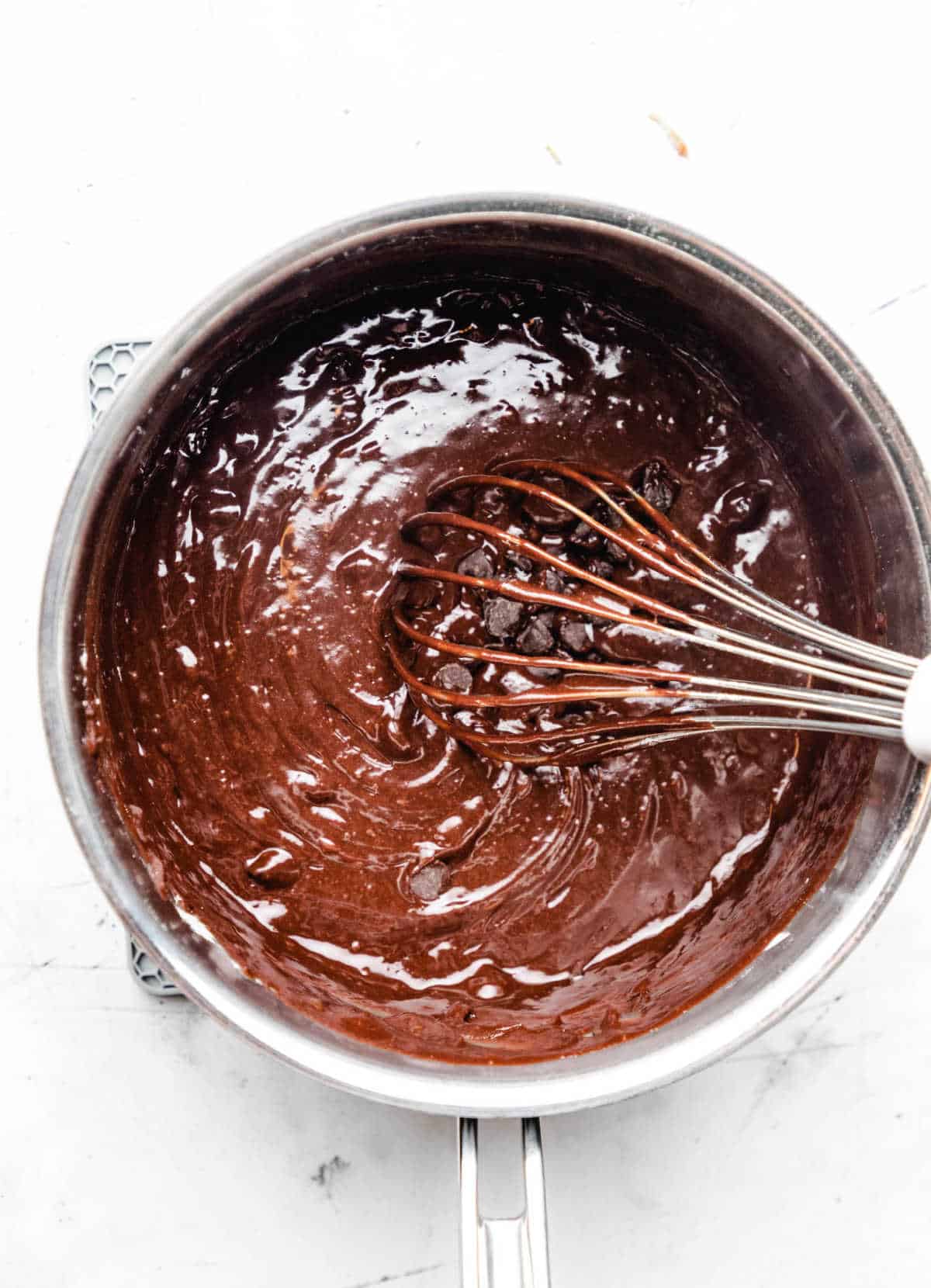 A whisk whisking chocolate chips into melted chocolate mixture. 