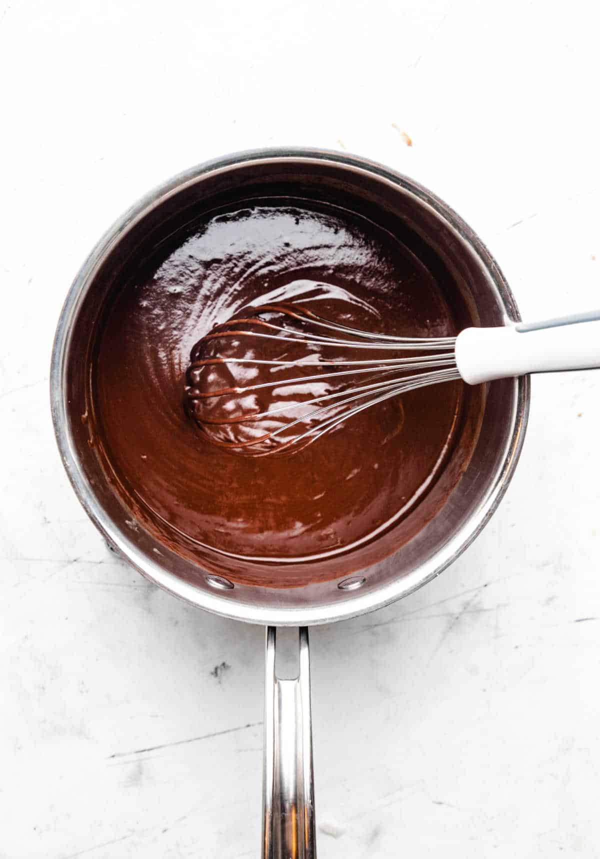 A whisk stirring chocolate chips into melted butter mixture. 