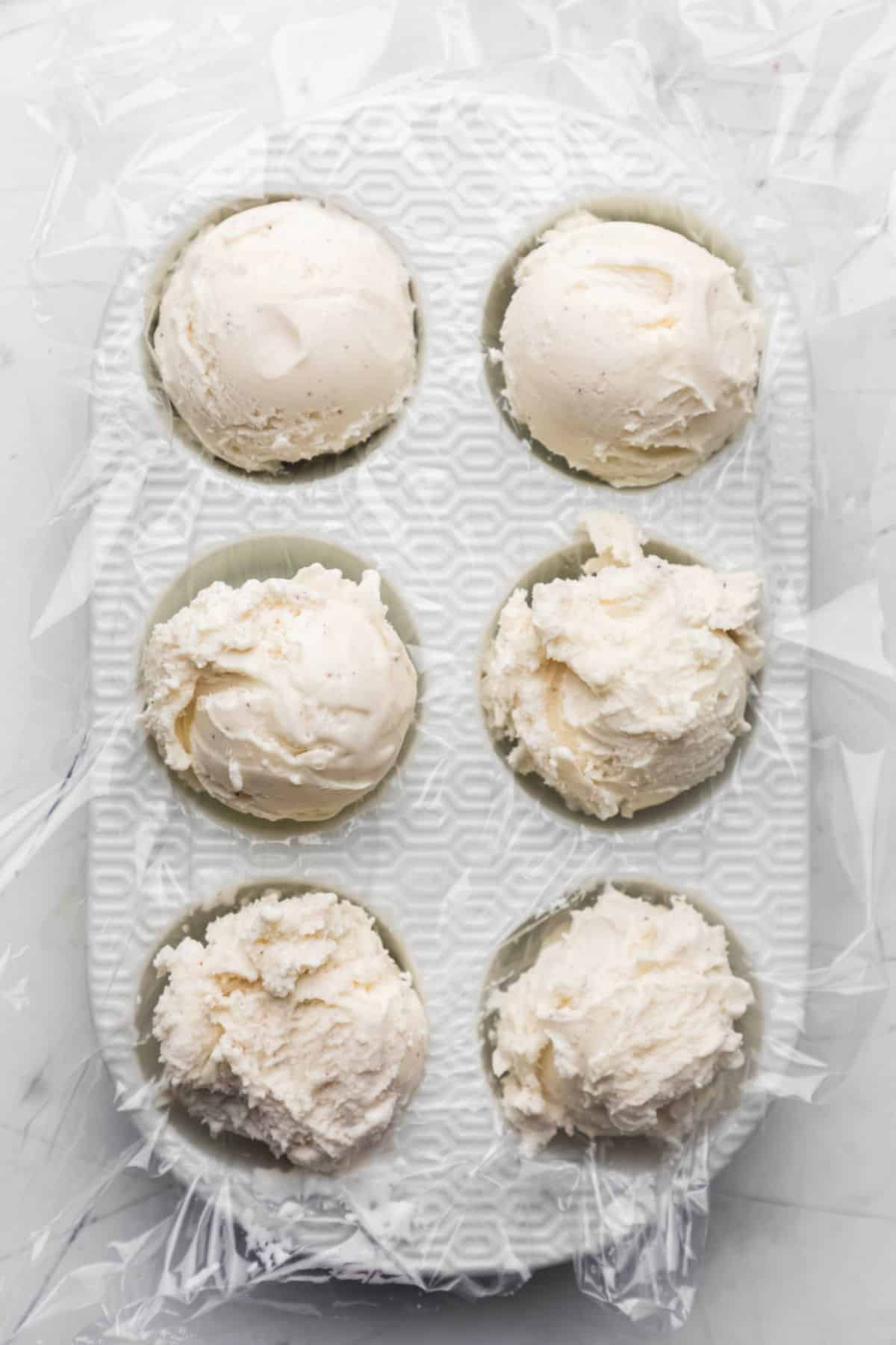 Six scoops of vanilla ice cream in a muffin pan.