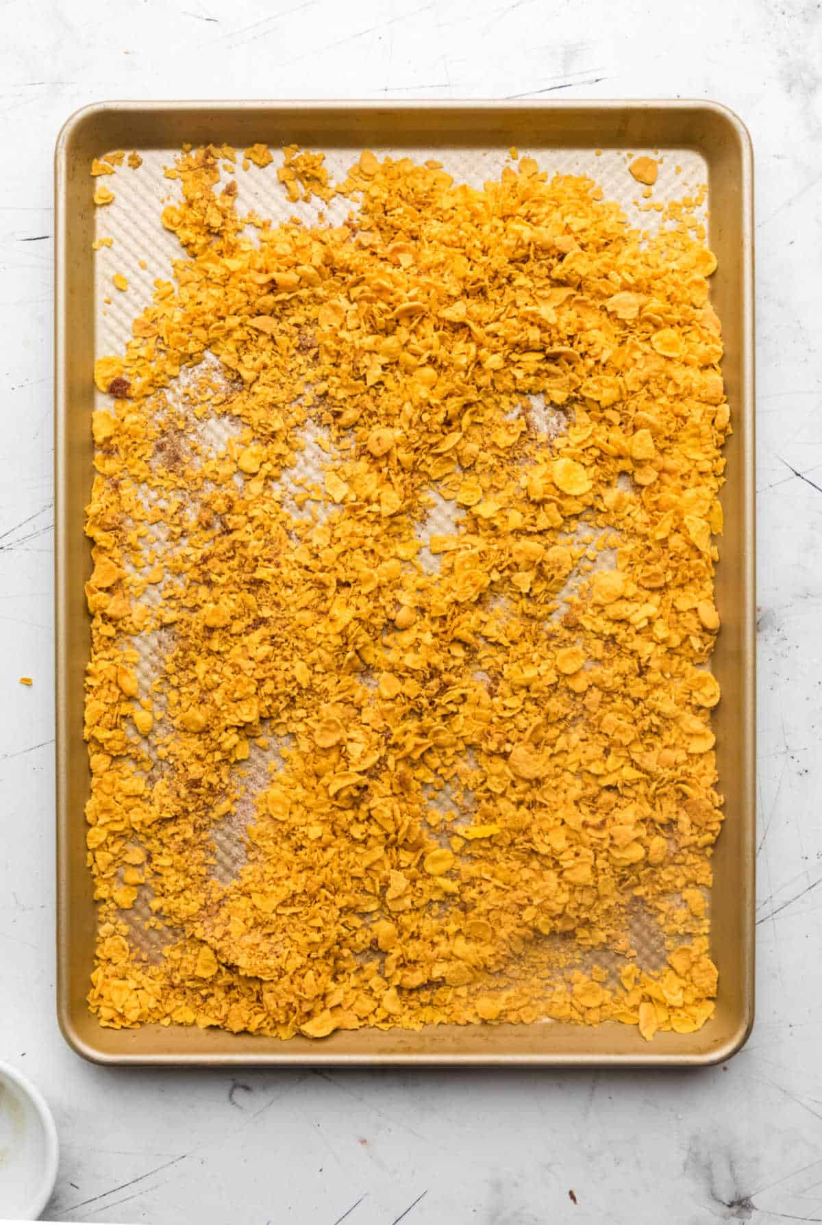 Crushed cornflakes, sugar, and cinnamon on a sheet pan.