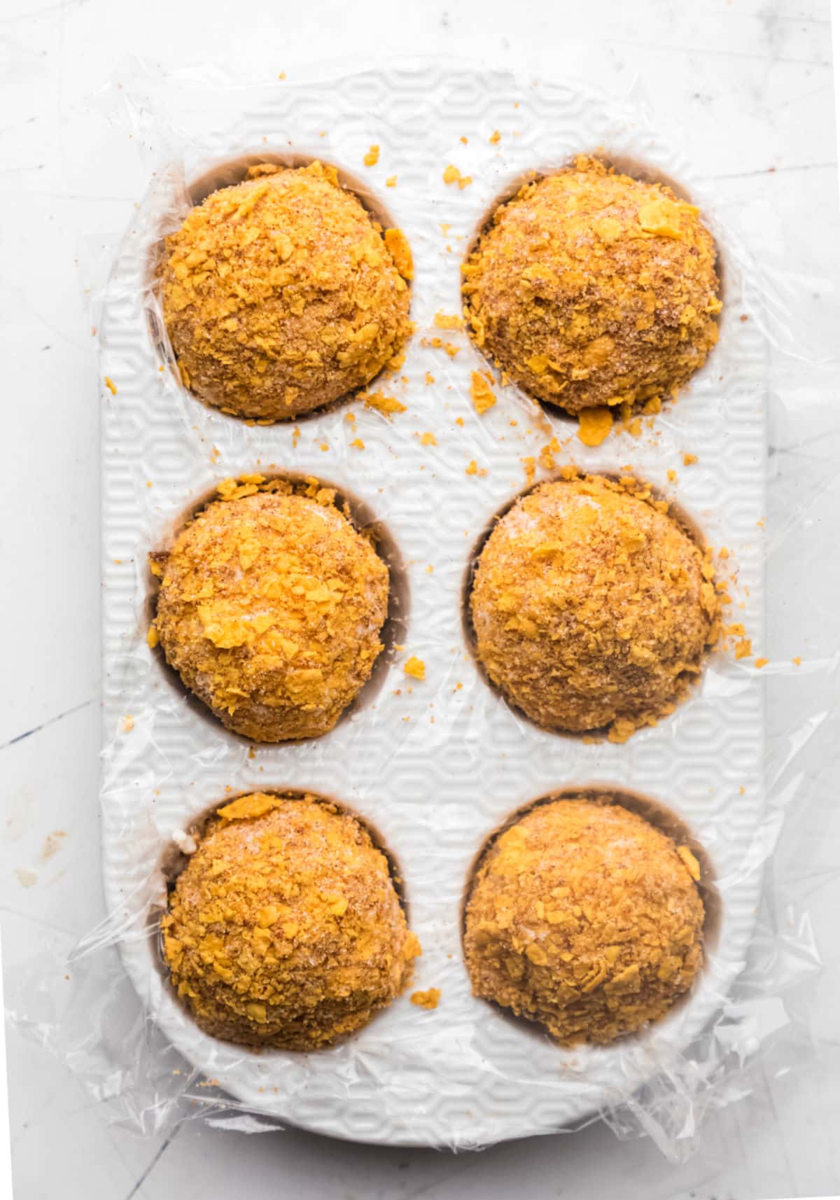 Six scoops of vanilla ice cream coated with cornflake mixture in a muffin tin.