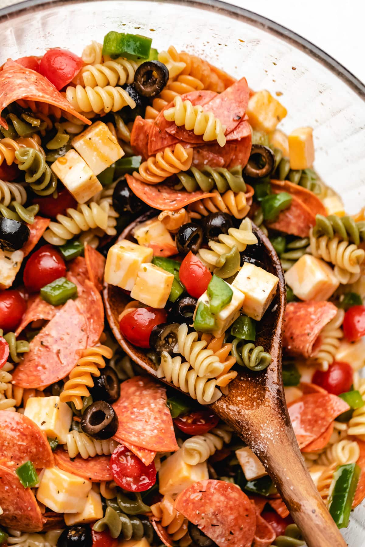 A wooden spoon with a scoop of pasta salad in a bowl of pasta salad. 