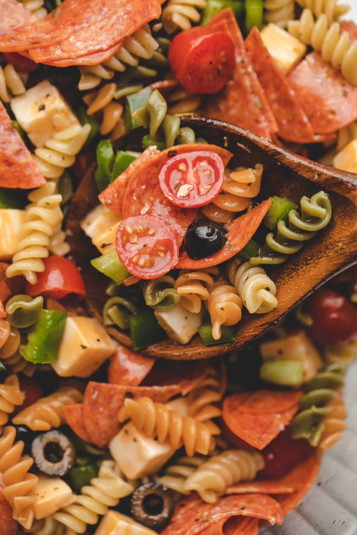 A wooden spoon holding a scoop of pasta salad. 