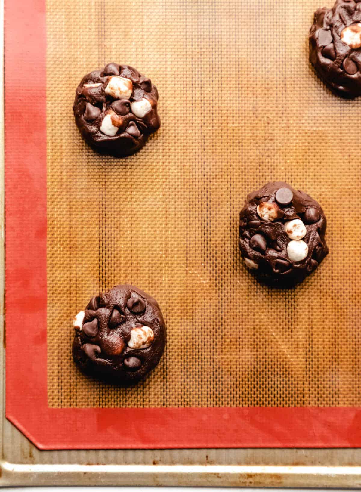 Scoops of rocky road cookie dough on a silicone baking mat. 