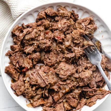 A plate of shredded slow cooker salsa verde beef next to a cream napkin.