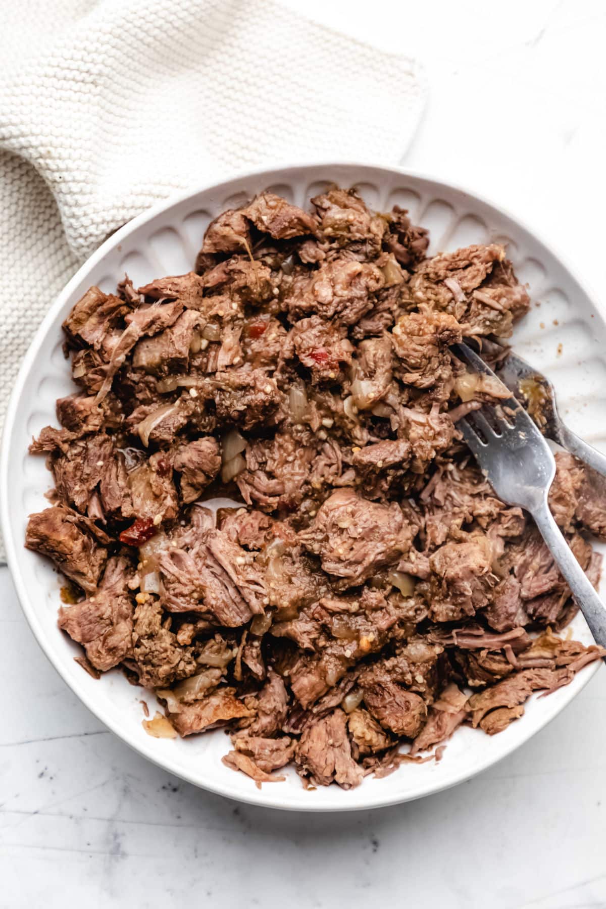 A plate of shredded slow cooker salsa verde beef next to a cream napkin.