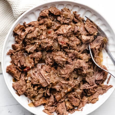 A white bowl with slow cooker salsa verde beef and a fork in it.