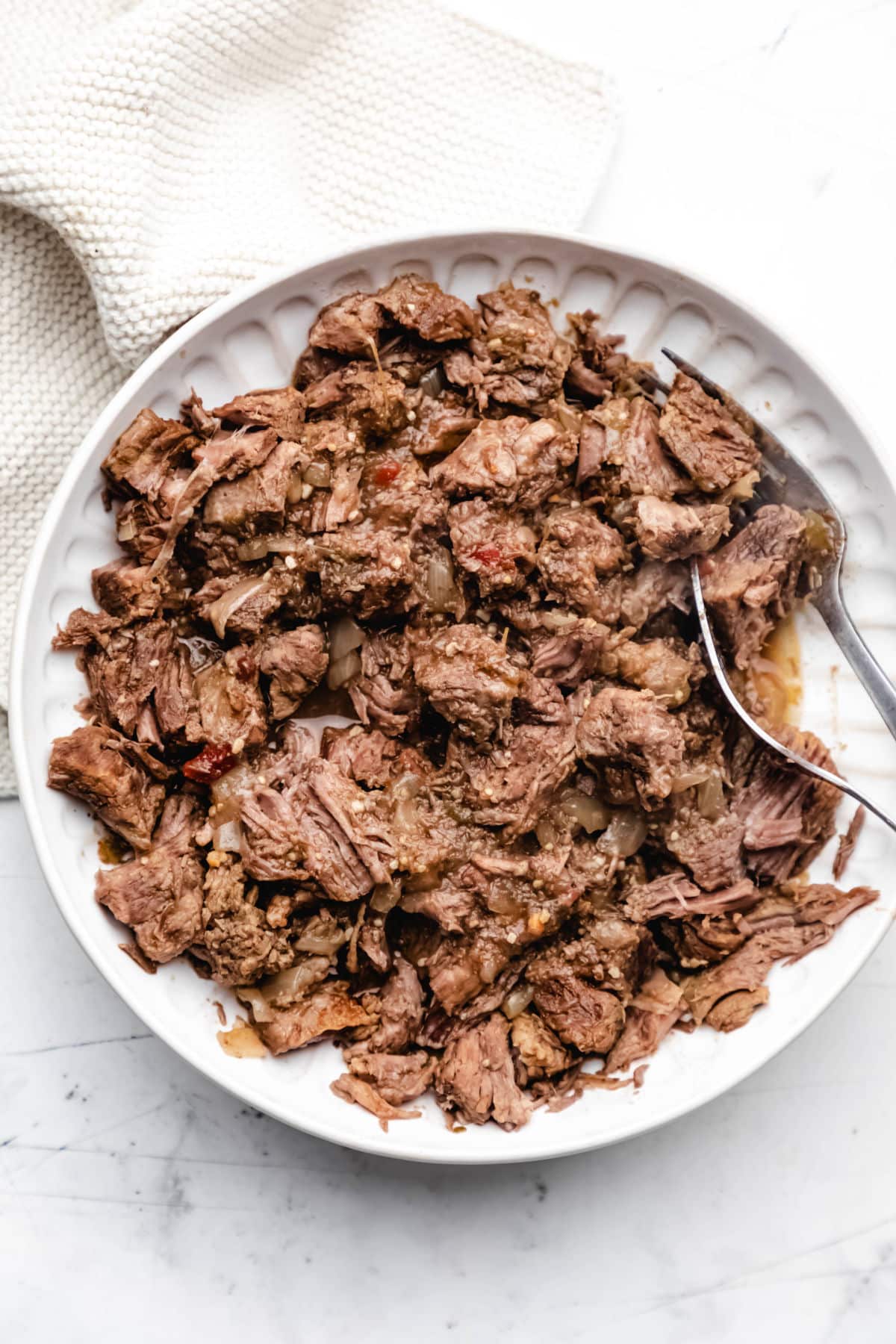 Slow cooker salsa verde beef shredded on a plate with two forks. 