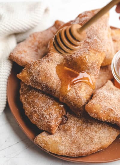 A honey dipper drizzling honey onto a stack of sopaipillas.