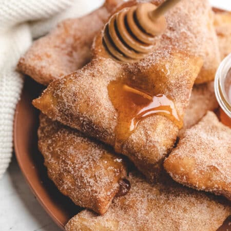 A honey dipper drizzling honey onto a stack of sopaipillas.