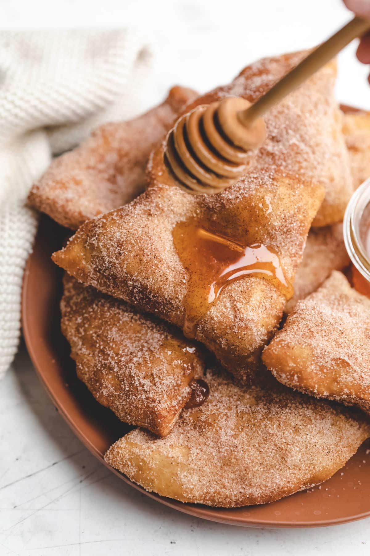 A honey dipper drizzling honey onto a stack of sopaipillas.