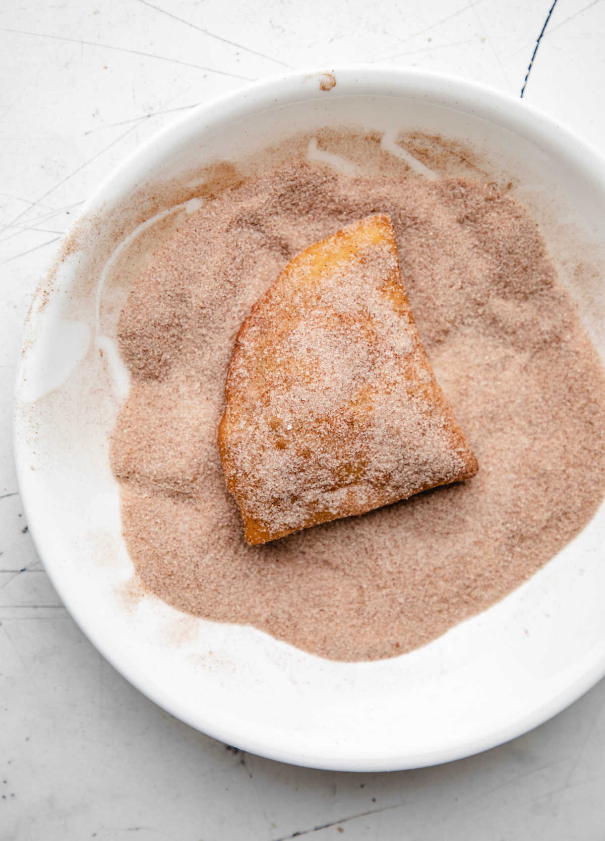 A sopaipilla in a dish of cinnamon sugar. 