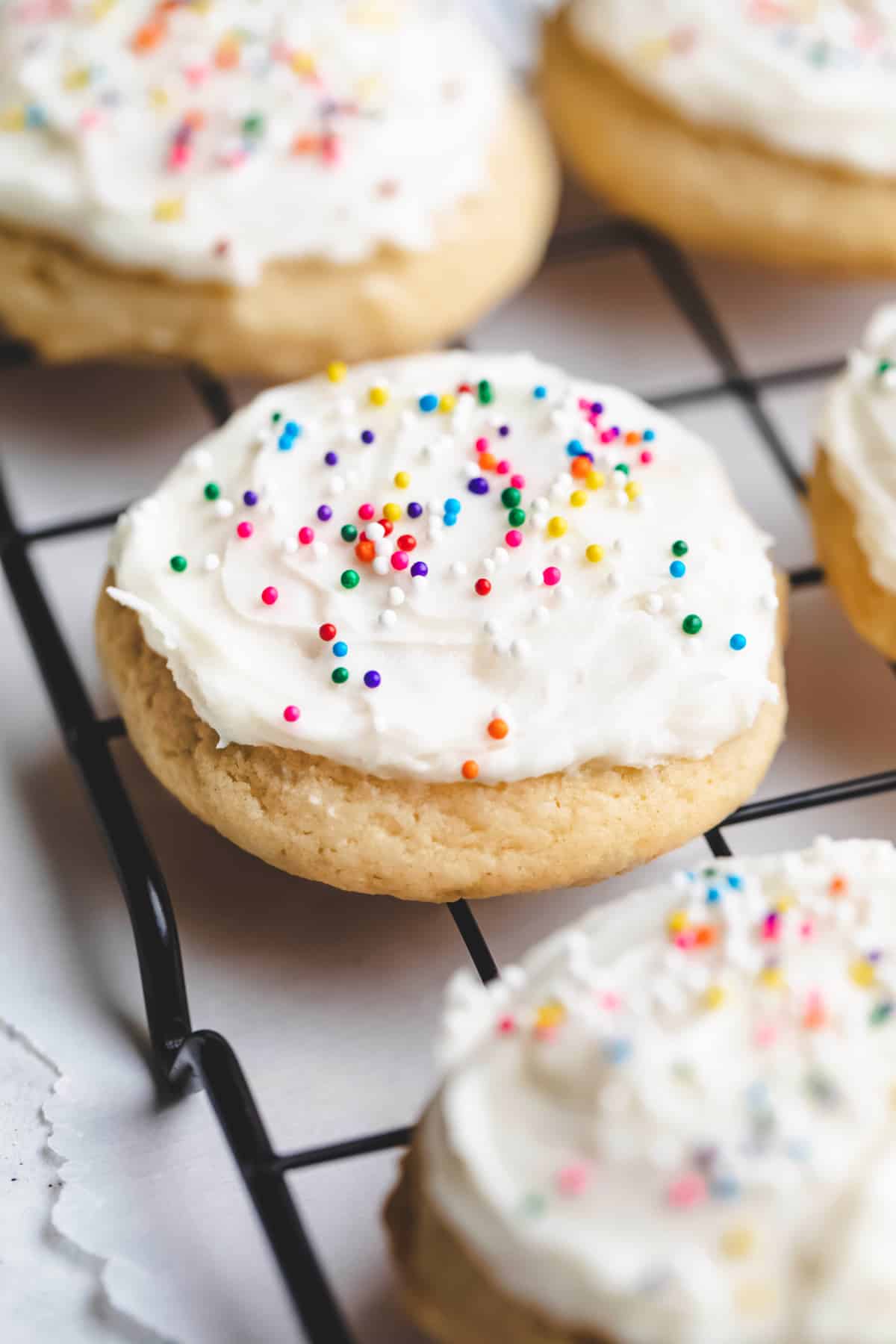 Rows of sour cream sugar cookies on a black wire cooling rack. 